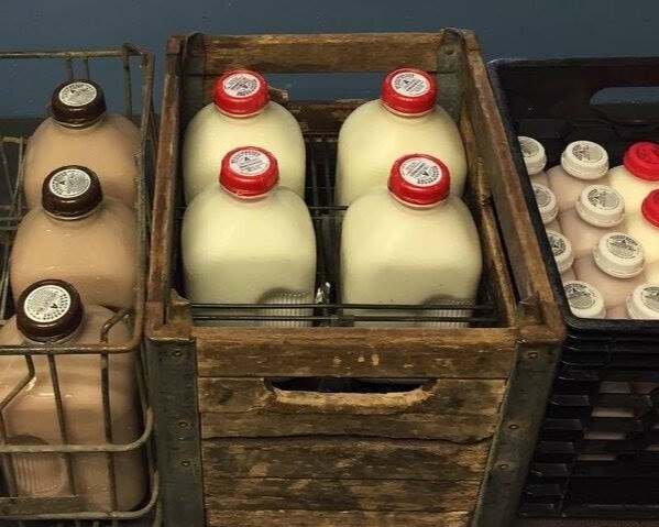 Wooden crate filled with glass bottles of milk and chocolate milk, showcasing a rustic display of dairy products in a market setting.