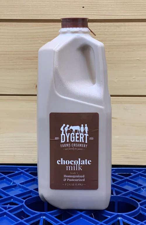 Container of Dygert Farms Creamery chocolate milk, showcasing a half-gallon plastic jug with a brown label indicating it is homogenized and pasteurized. The background features wooden planks and a blue crate.