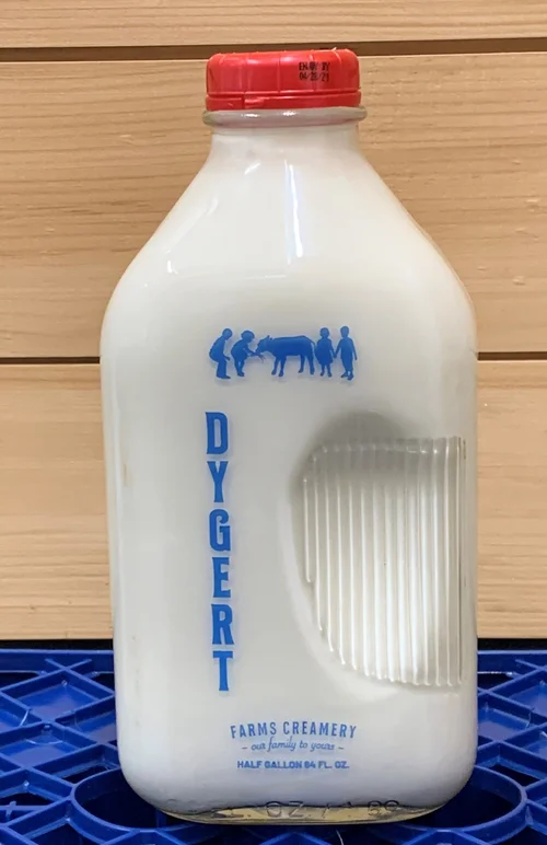 Half-gallon bottle of Dygert Farms Creamery milk with a red cap, featuring a blue label and graphic of people interacting with a cow, placed on a blue plastic crate.