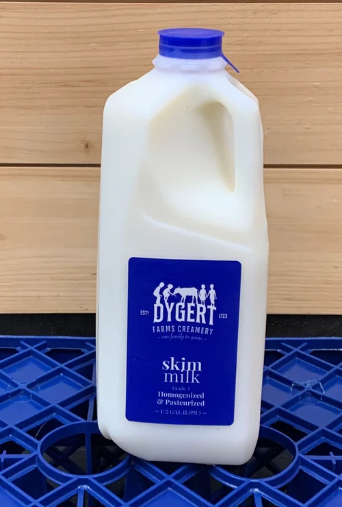 Skim milk in a white plastic jug with a blue cap, labeled Dygert Farms Creamery, featuring the text "skim milk, homogenized & pasteurized" and established 1723, placed on a blue plastic crate.