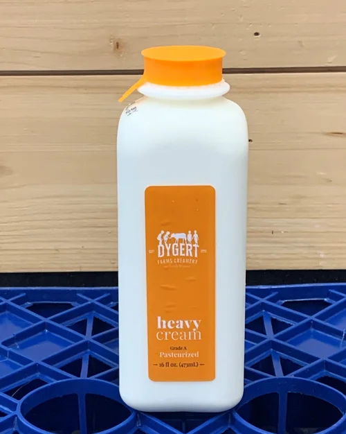Bottle of Dygert Farms creamy heavy cream, 16 fl oz, with an orange cap and label, displayed against a wooden background and blue crate. Ideal for cooking and baking.