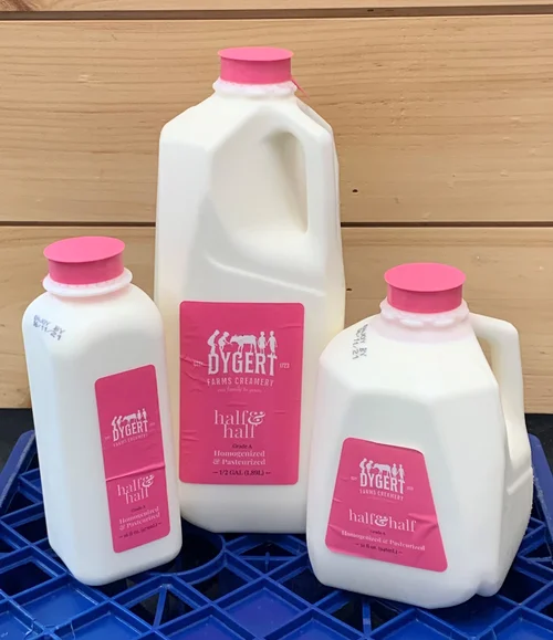 Three containers of Dygert Farms Creamery half and half, featuring pink lids and labels, displayed on a blue crate against a wooden background.