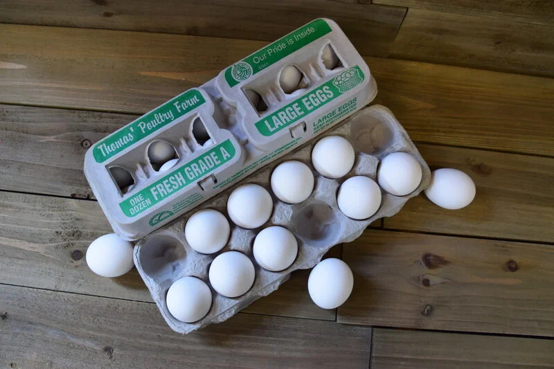 Fresh large eggs in a carton labeled "Thomas' Poultry Farm," showcasing a dozen eggs on a rustic wooden surface. The carton highlights "Fresh Grade A" quality, emphasizing farm-fresh produce.